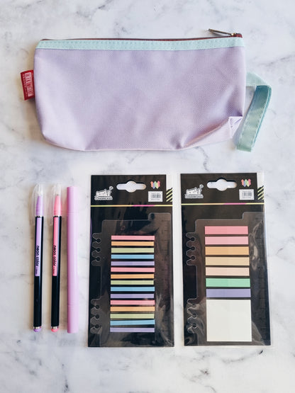 A pastel highlighter, two colorful pens, a pack of sticky tabs, a mini pack of sticky tabs, and a pastel pencil case, all laid out on a marble surface.